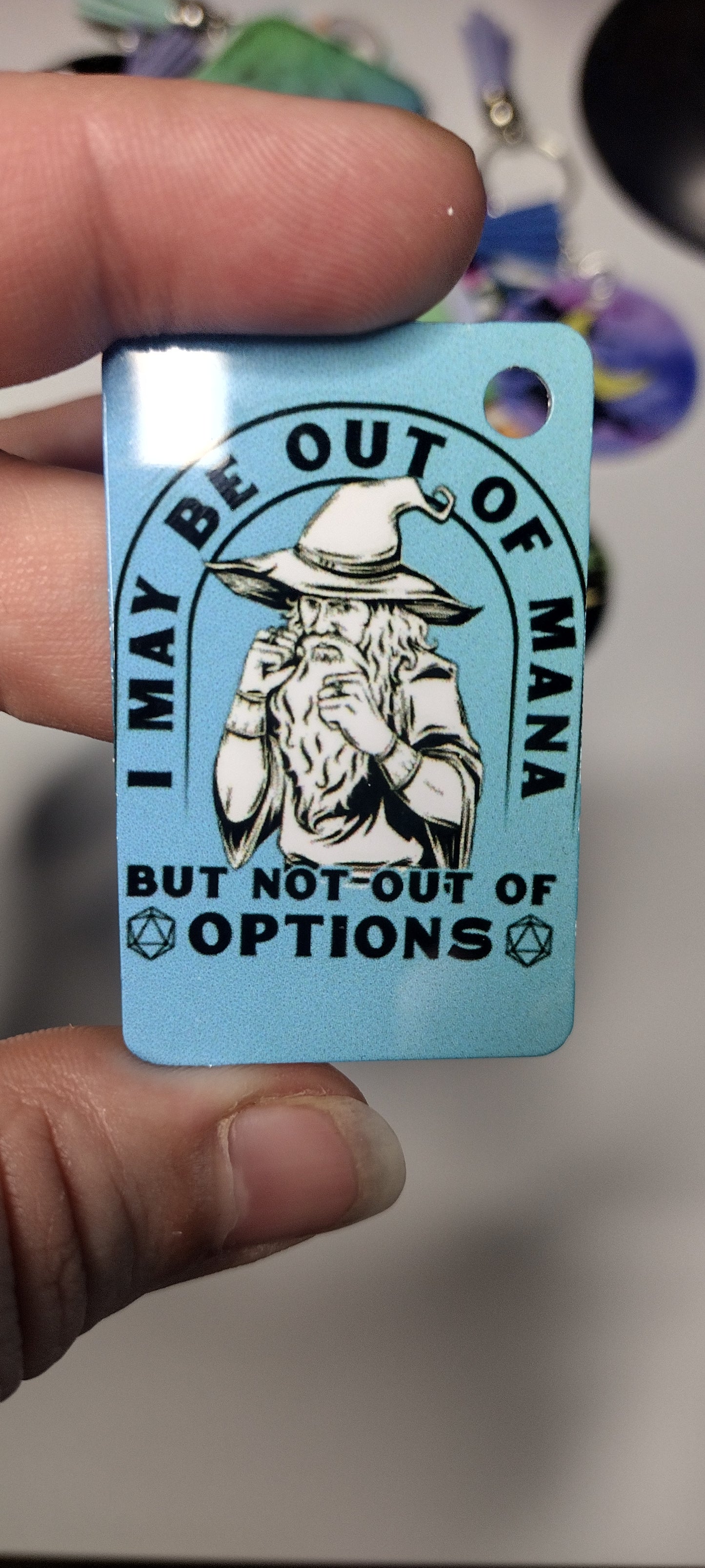 Blue key chain, imperfectly aligned. Wizard with fists up and the phrase I may be out of mana but not out of options.